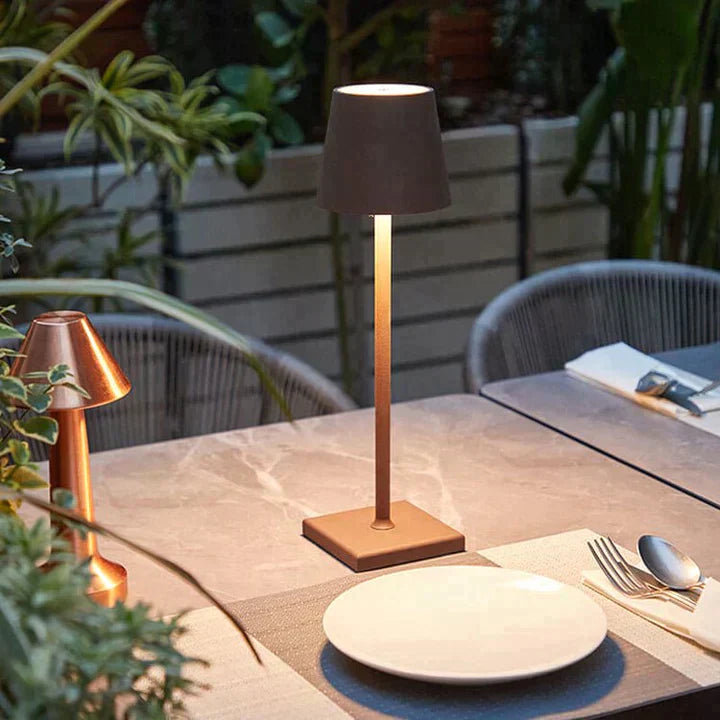 Lampe Luminelle brune allumée sur une table de terrasse entourée de plantes