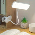 Lampe Clipéa blanche fixée à une étagère et allumée au-dessus d’un livre.