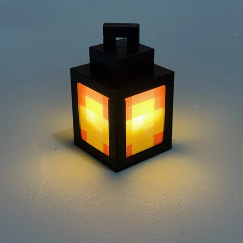 Lanterne Pixelia Mini noire diffusant une lumière orangée sur fond gris.