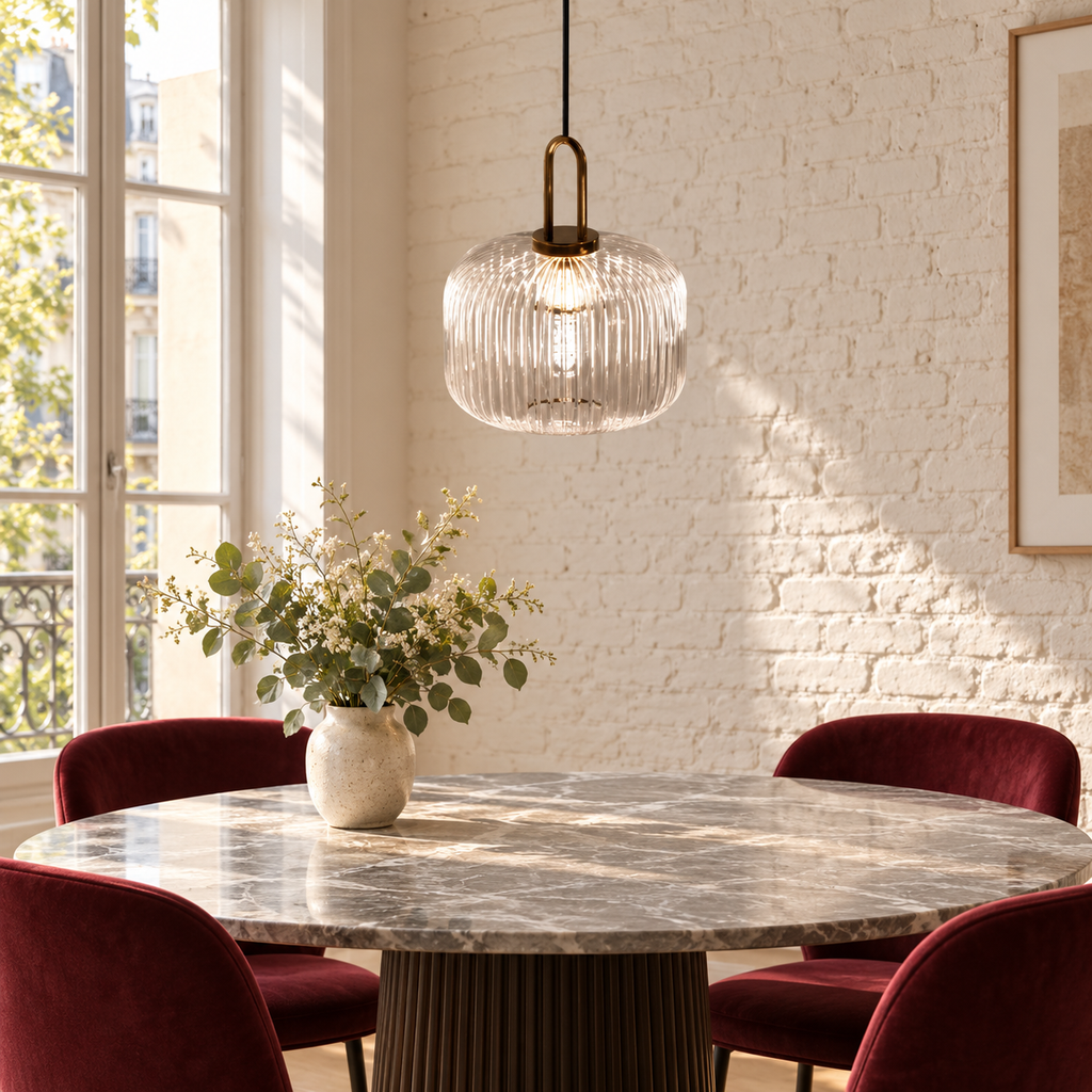 Suspension en verre côtelé dans un décor illustratif au-dessus d'une table ronde avec plateau marbre gris et chaises bordeaux dans un coin repas français lumineux