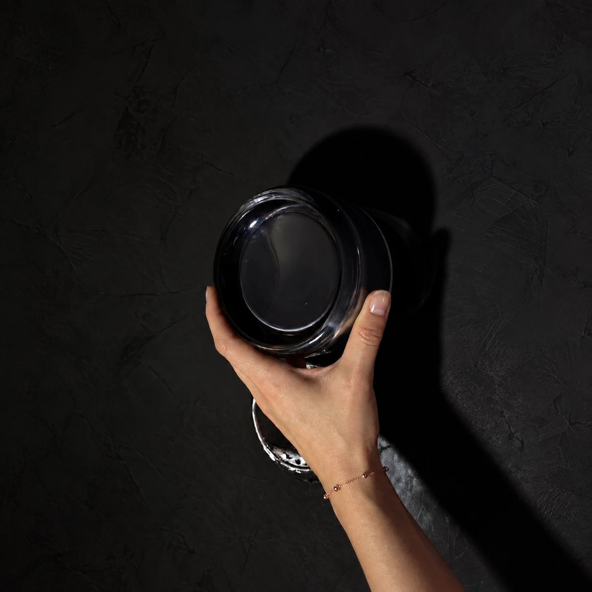 Evoa sombre tenue dans une main devant un mur noir — cadrage retouché.