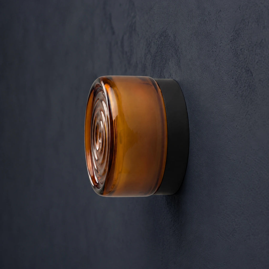 Evoa ambrée en vue de profil : diffuseur rond à cercles concentriques sur une base sombre — cadrage retouché.
