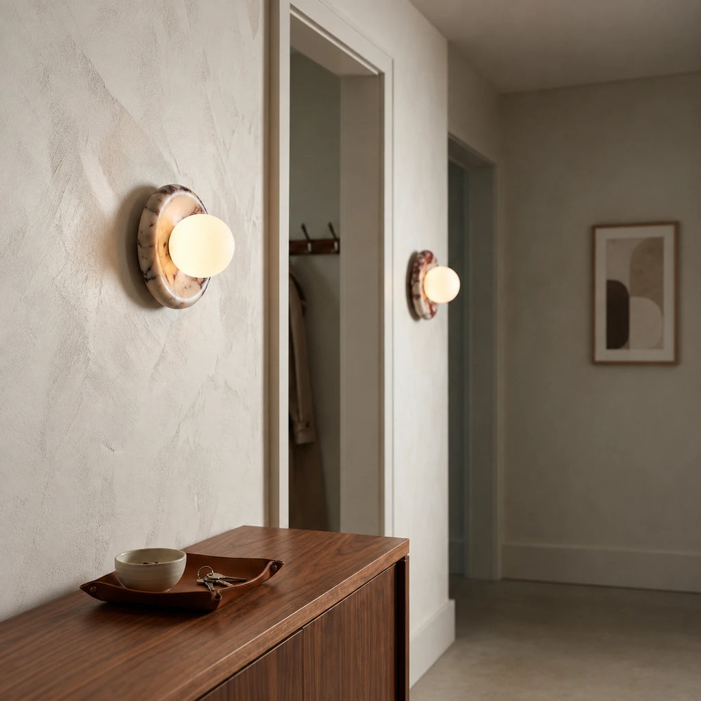 Rubi : deux appliques allumées à globe blanc et disque marbré dans un couloir avec console en bois — cadrage retouché.