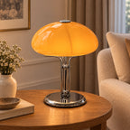 Girolle — lampe à dôme orange et pied chromé, sur une table près d’un fauteuil clair — mise en scène illustrative
