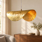 Suspension feuille de lotus dorée dans un décor illustratif au-dessus d'une console de noyer dans un salon aux murs écrus avec rideaux en lin et fauteuil gris discret