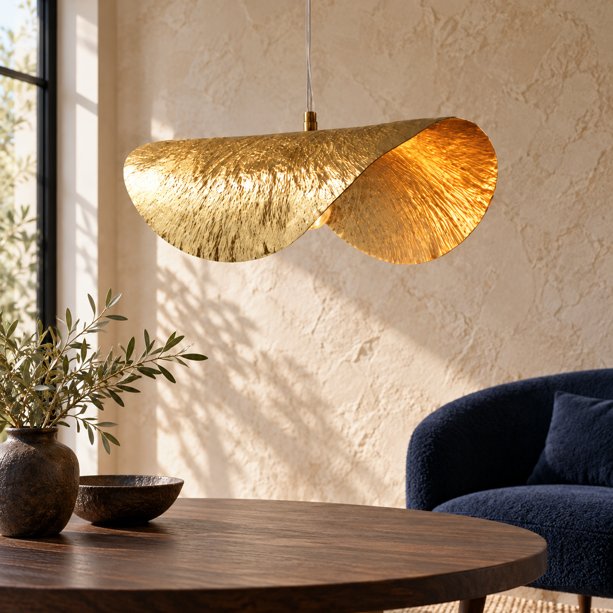 Suspension feuille de lotus dorée dans un décor illustratif dans un petit salon avec mur à relief minéral beige et fauteuil tapissé bleu nuit