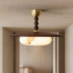 Plafonnier Bosquet allumé, vu de face dans un couloir, avec disque en bois foncé et trois sphères décoratives.