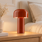 Dôme rouge, lampe de table nomade sur un chevet en bois clair.