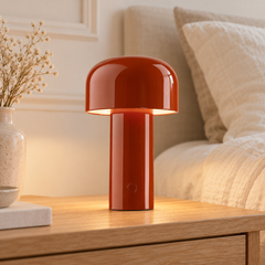 Dôme rouge, lampe de table nomade sur un chevet en bois clair.