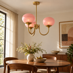 Guimauve — lustre à trois globes roses et structure dorée au-dessus d’une table
