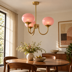 Guimauve — lustre à trois globes roses et structure dorée au-dessus d’une table