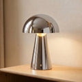 Chromelle — lampe chromée à dôme arrondi et pied conique avec bouton rond, allumée sur un meuble en bois