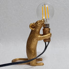 Lampe souris dorée debout tenant une ampoule, vue de profil.