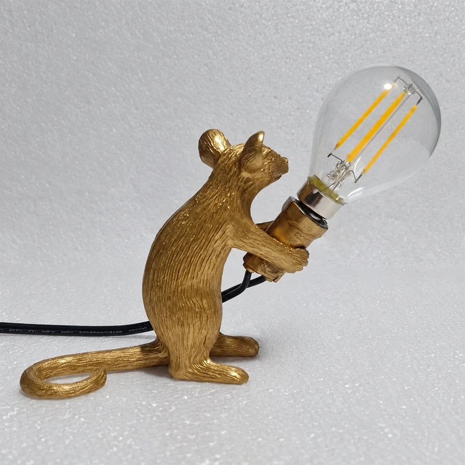 Lampe souris dorée assise tenant une ampoule inclinée, vue de profil.