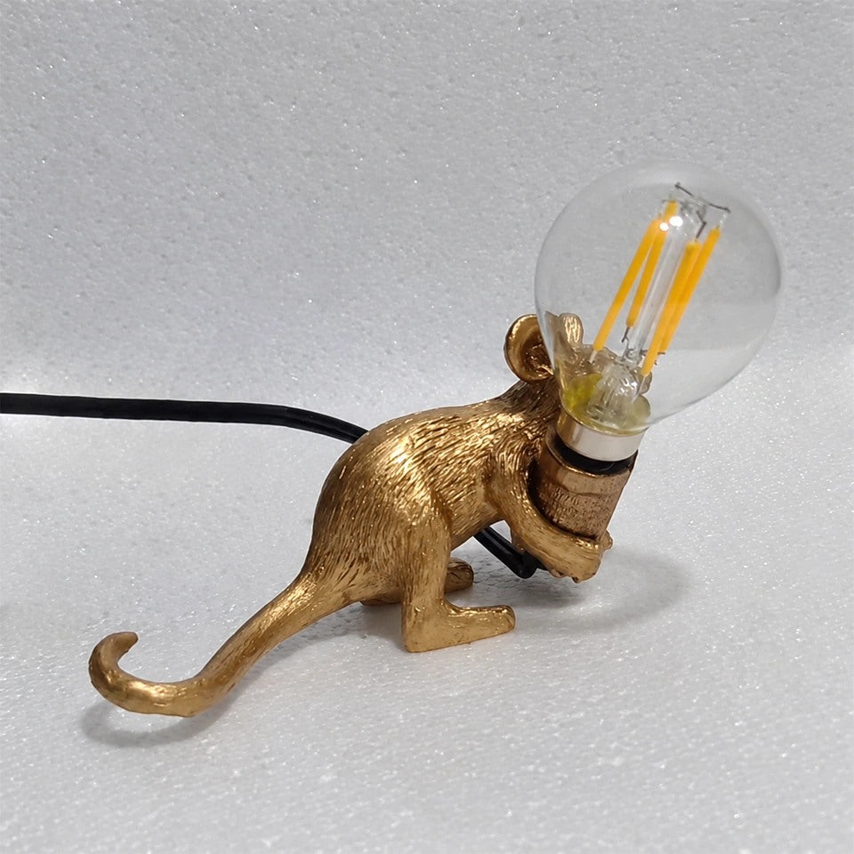 Lampe souris dorée allongée tenant une ampoule, vue de trois quarts.