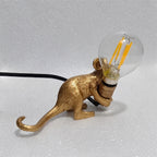 Lampe souris dorée allongée tenant une ampoule, vue de trois quarts.